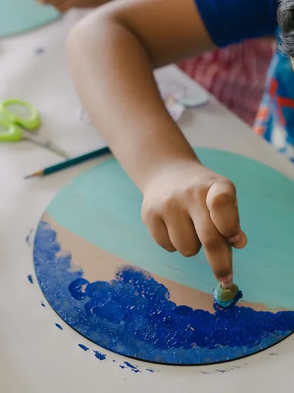 Finger painting isn't just for toddlers! Here, a student uses their finger to blend colors on a wooden circle. I encourage kids to experiment with different tools and techniques to create unique textures in their art.
