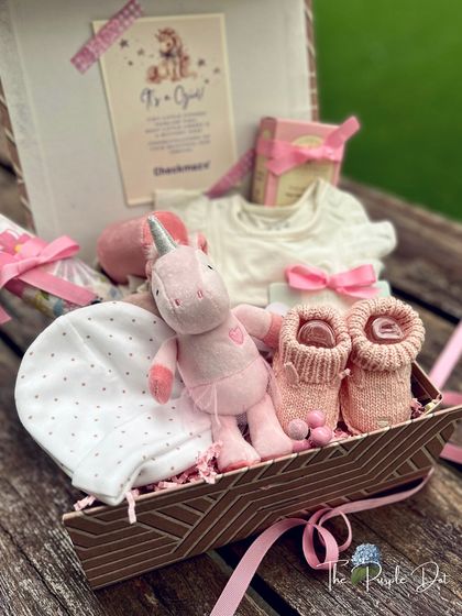 A unicorn-themed hamper for a baby girl, featuring a sweet unicorn plush, matching booties, and a soft onesie, all tied together with delicate pink ribbons.