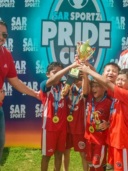 Young champions in red jerseys shout with joy as they lift the Pride Cup trophy.