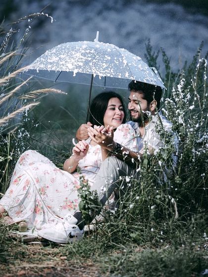 A sweet, interactive moment under an umbrella, with the couple looking at each other amidst falling snow.