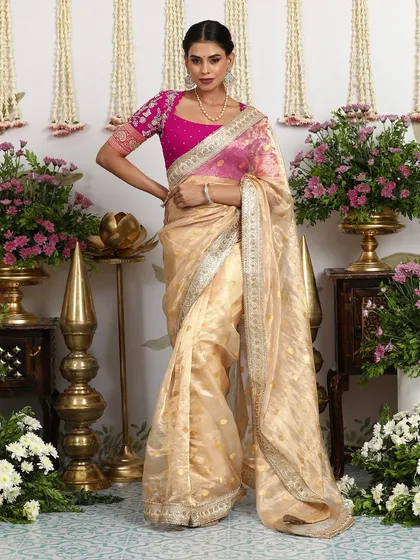 A muted gold Banarasi silk saree with a sheer organza feel, paired with a fuchsia pink Bandhani blouse.