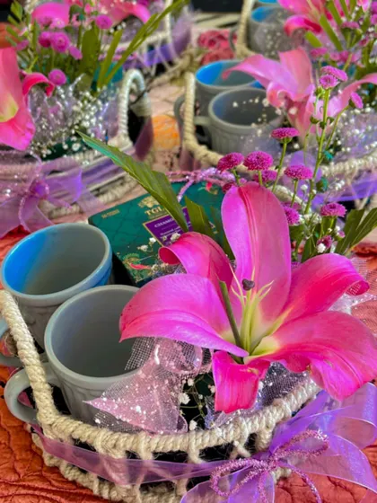 Multiple tea and mug favour baskets ready for an event. The arrangement showcases bright pink lilies, purple ribbons, and sparkling tulle, creating a cohesive and visually stunning set of gifts for guests.