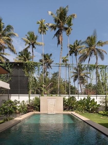 Looking across the pool at Villa Shakthi, you can see how the design uses clean lines and natural materials to complement the surrounding palm trees and tropical foliage. The water acts as a reflective surface, enhancing the serene atmosphere of this private residence.