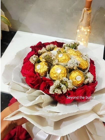 A stunning bouquet featuring a heart of Ferrero Rocher chocolates surrounded by a ring of fresh red roses, all wrapped in elegant white paper.