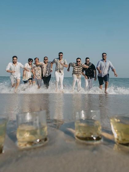A fun shot of the groomsmen running into the ocean in Goa, with their drinks waiting on the sand. This captures the playful and adventurous spirit of a destination wedding.