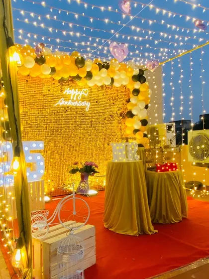 This is a full view of a 25th-anniversary terrace decoration. The space is defined by a red carpet, a golden shimmer wall, and a canopy of fairy lights, creating a glamorous entrance and party area.
