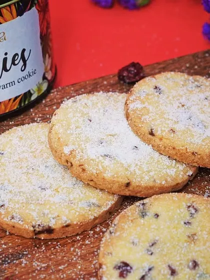 A close-up of 'reeva' brand cookies on a wooden board, dusted with sugar. This rustic styling gives the product a warm, homemade feel, perfect for artisanal brands.