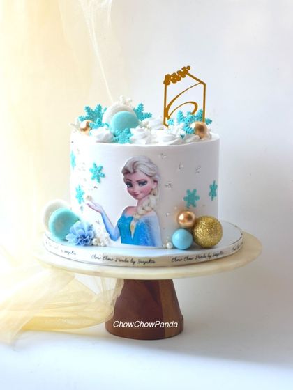 A wintery Elsa cake from Frozen for a 6th birthday. This Choco Vanilla cake is decorated with an edible image of Elsa, buttercream snowflakes, and macarons.