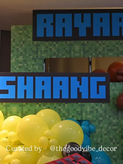 Custom name signs in the classic Minecraft font, placed against a pixelated green backdrop to personalize the gaming-themed birthday party.