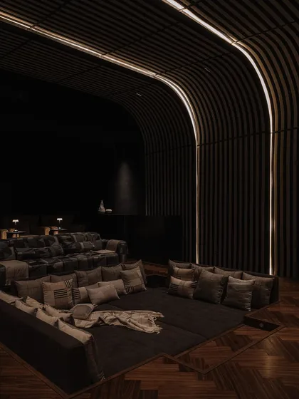 A glimpse into the dedicated home theatre at Rehethaan. We designed the space with curved, slatted walls and plush, tiered seating to create an immersive and luxurious cinematic experience for the family.