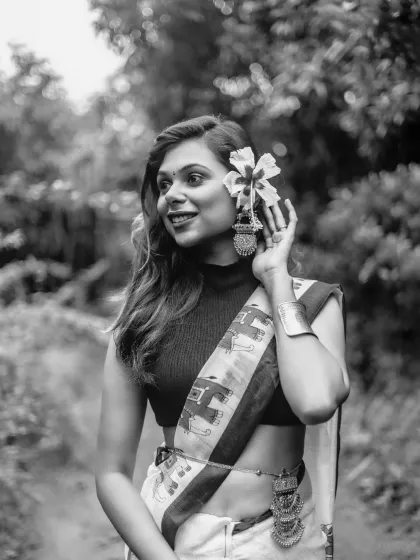 A black and white portrait highlighting the details of the model's accessories, from the flower in her hair to her traditional earrings and belt.