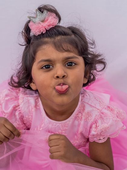 A candid moment of a little girl feeling like a princess in her pink dress. The crown hair accessory completes this adorable and playful party look.