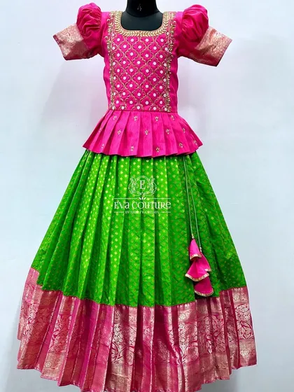 A vibrant combination of parrot green and rani pink. The blouse has a grid pattern embroidery, and the skirt has a traditional pink and gold border.