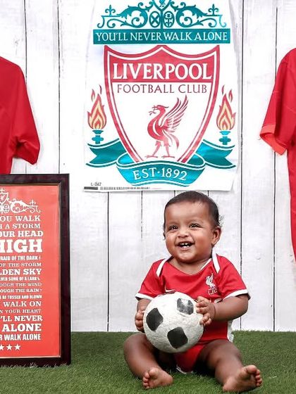 A wide shot of the Liverpool FC setup, showing the team jerseys, poster, and a very happy little fan.