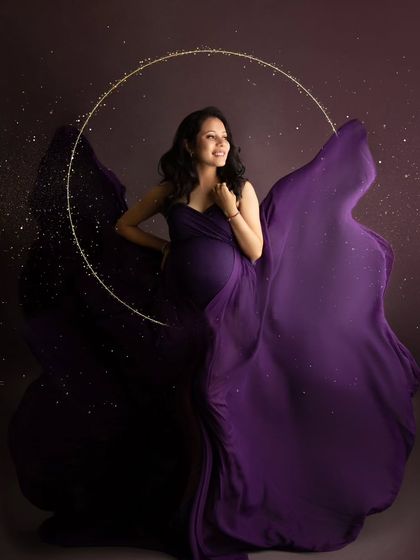 A smiling, happy portrait of a mom-to-be in a flowing purple gown, surrounded by a magical halo and sparkling lights.