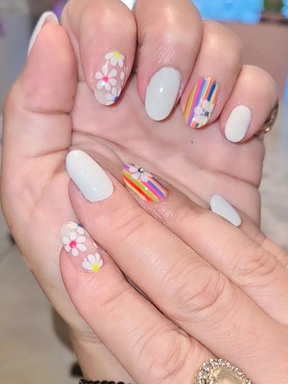 A chic and summery design featuring white nails with accent nails of hand-painted daisies and colorful rainbow stripes.