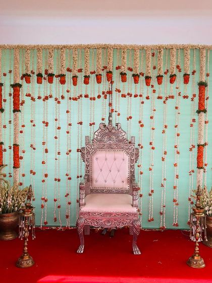 A simple yet elegant backdrop with a light blue wall, decorated with hanging strings of jasmine and orange marigolds.