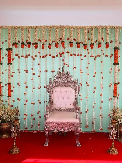 A simple yet elegant backdrop with a light blue wall, decorated with hanging strings of jasmine and orange marigolds.