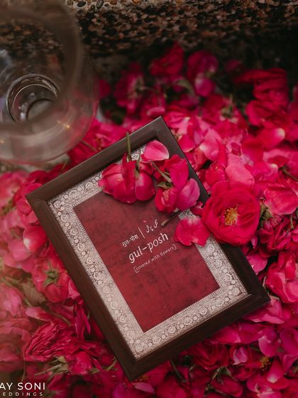 A framed sign defining "gul-posh" (covered with flowers), perfectly describing the essence of the event, laid on a bed of vibrant red flowers.