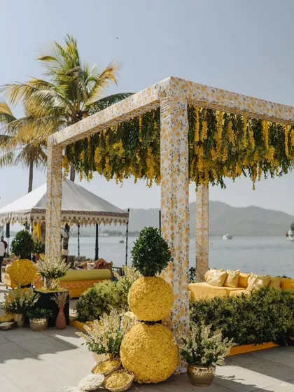 A chic and sunny Haldi setup by the lake in Udaipur. The yellow floral canopy and comfortable seating create a relaxed yet elegant atmosphere for this pre-wedding ritual.