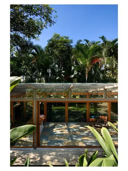 From an elevated viewpoint, the glass roof reflects the sky and surrounding trees, further merging the structure with its environment.