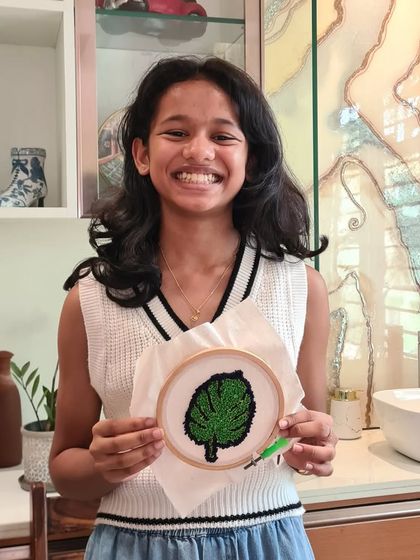 A young artist proudly presenting her completed green leaf punch needle project.