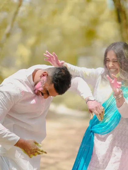 This candid shot captures the energy and laughter of a couple mid-play, dodging and throwing colored powder during their fun pre-wedding session.