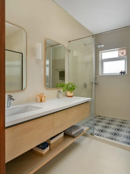 A bathroom from our 'House of Kismish' project, featuring a double vanity with a light wood finish and patterned floor tiles in the shower area.