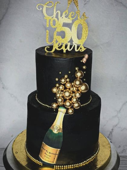 Turning half a century old calls for a celebration, and a cake from me! This two-tiered black and gold 50th birthday cake features a champagne bottle theme with edible golden bubbles.