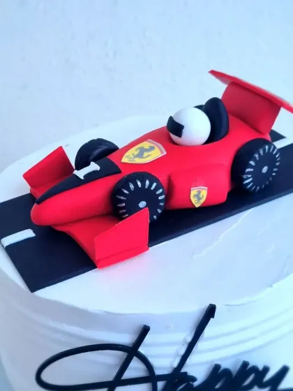 A close-up of the sculpted fondant Ferrari on a whipping cream cake, highlighting the details of the car.