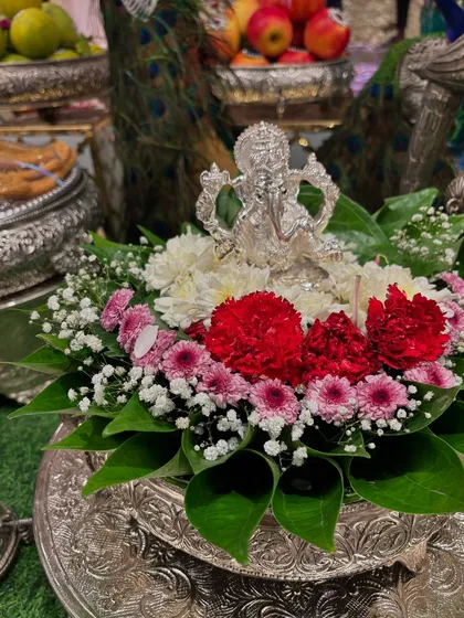 A small silver Ganesha idol placed on betel leaves and adorned with fresh red and pink flowers.