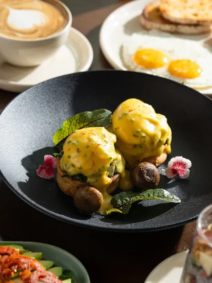 A beautifully plated eggs benedict on a dark plate, which makes the yellow hollandaise sauce stand out.