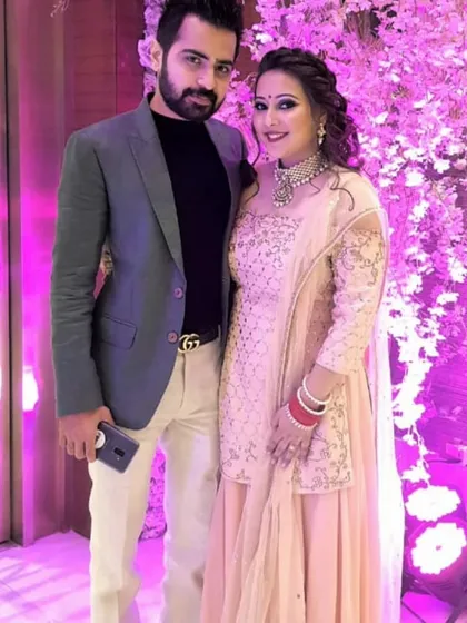 A happy couple at a wedding function. The client is wearing a beautiful peach sharara set by Pooja Peshoria, featuring delicate silver embroidery, perfect for a guest or for pre-wedding festivities.