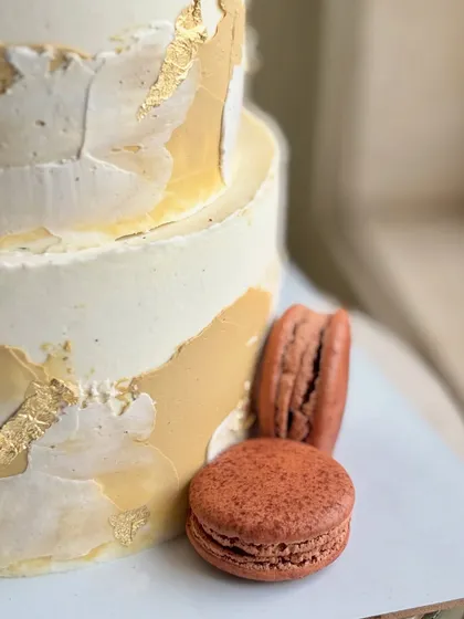 A side view highlighting the beautiful contrast between the rustic buttercream, the luxe gold leaf, and the smooth surface of the macarons at the base.