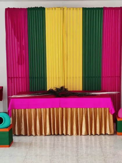 A clear, straight-on view of the completed Janamashtmi backdrop and table. The peacock feathers are placed on the table, ready for the final idol placement.