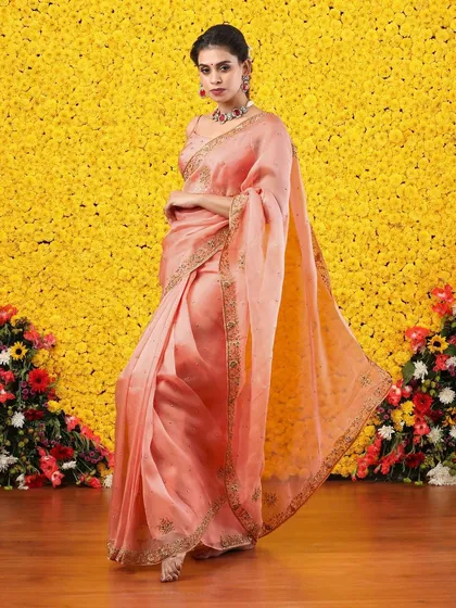 The flowing pallu of the peach organza saree creates a look of effortless grace.