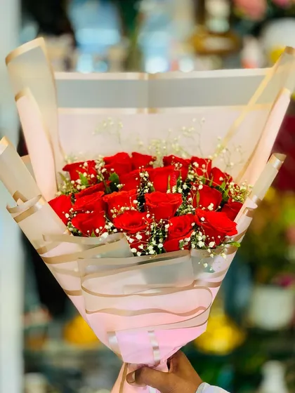 A generous bouquet of red roses and baby's breath, presented in a modern Korean-style wrap. The semi-transparent paper with gold stripes adds a layer of sophistication.