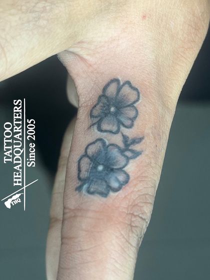 Two small, simple flower tattoos on the thumb, a delicate and nature-inspired design.
