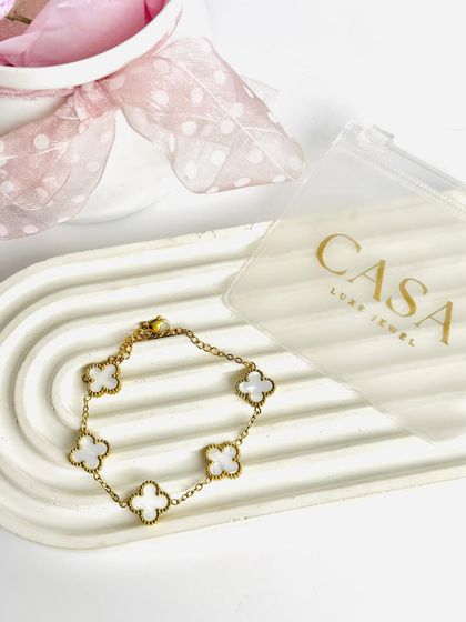 A minimalist flatlay of a clover-charm bracelet on a modern, arched tray. The clean composition and soft props make this a perfect shot for a chic, contemporary brand.