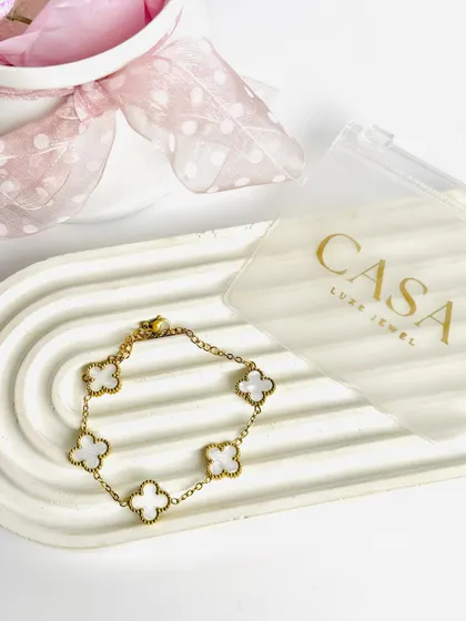 A minimalist flatlay of a clover-charm bracelet on a modern, arched tray. The clean composition and soft props make this a perfect shot for a chic, contemporary brand.