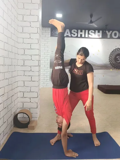 Assisting a student with a wall-supported handstand. This one-on-one guidance helps the student understand the alignment and balance required for the full pose.