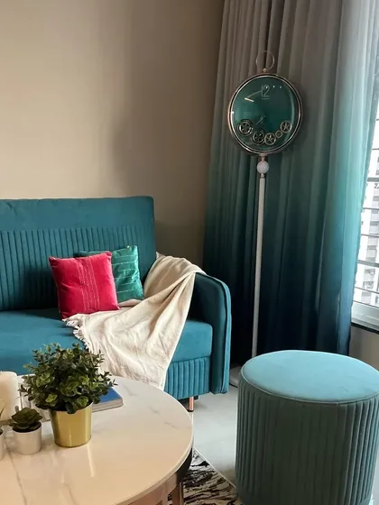 A cozy corner in a living room featuring a teal sofa, matching ottoman, and ombre curtains. The unique floor clock adds a whimsical and artistic touch to the space.