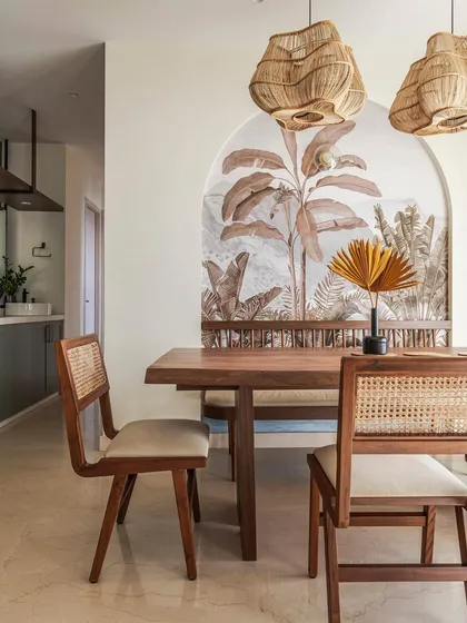 The dining area is a perfect blend of natural textures and traditional craftsmanship. A live-edge wooden table is paired with cane-backed chairs, set against a stunning tropical wallpaper mural that acts as a focal point within an arched niche.
