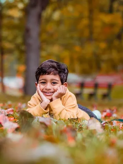 An adorable shot of a young boy lying in a bed of autumn leaves with a charming smile. The vibrant fall colors and his joyful expression make this a standout portrait.