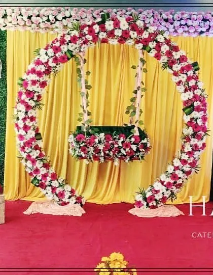 We design elegant stage setups like this one, featuring a circular floral arch that frames the baby's cradle. The combination of a lush greenery wall, soft drapery, and warm lighting creates a beautiful photo backdrop.