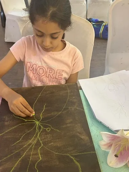 A student begins her Georgia O'Keeffe-inspired piece by drawing with chalk on a dark canvas. This helps in planning the composition before adding layers of vibrant acrylic paint.