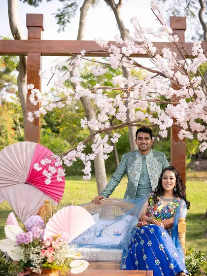 The couple posing at their photo-op, complete with paper fans and a cherry blossom tree.