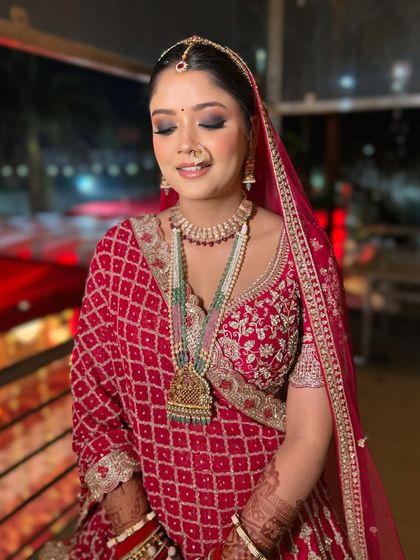 A beautiful bride in a traditional red bandhani outfit. The makeup features a classic smokey eye and a dewy base to create a stunning look for her night ceremony.