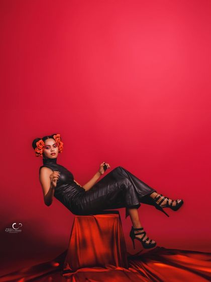 A relaxed yet powerful pose. The contrast between the black leather, red flowers, and red background is visually stunning.
