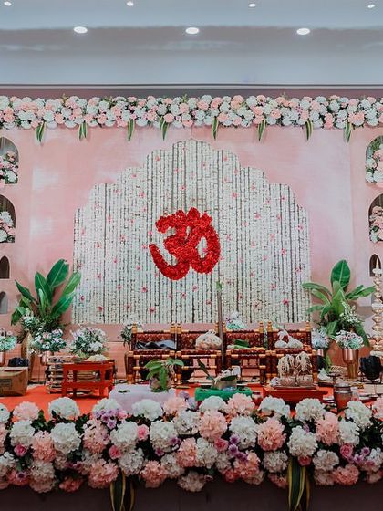 The beautiful stage decor for a traditional wedding ceremony, featuring a pink backdrop, an Om symbol made of flowers, and lush floral arrangements.
